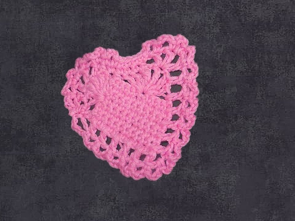 Gehäkeltes rosa Herz mit Spitzenrand auf dunklem Hintergrund