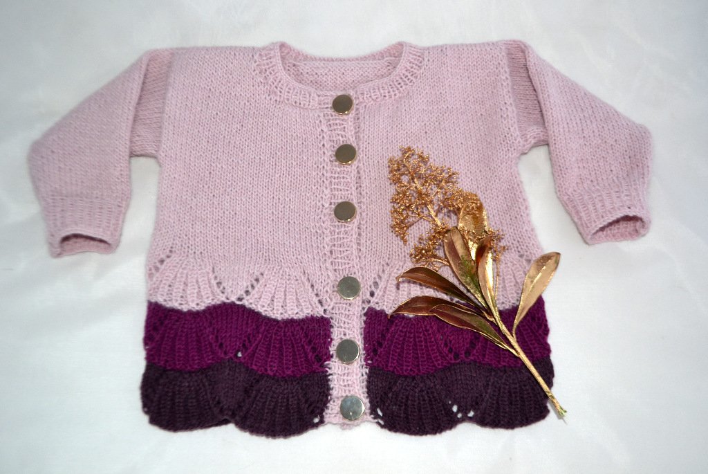 Rosa gestrickte Babyjacke mit dreifarbiger Muschelkante (lila, dunkelviolett) und runden Metallknöpfen