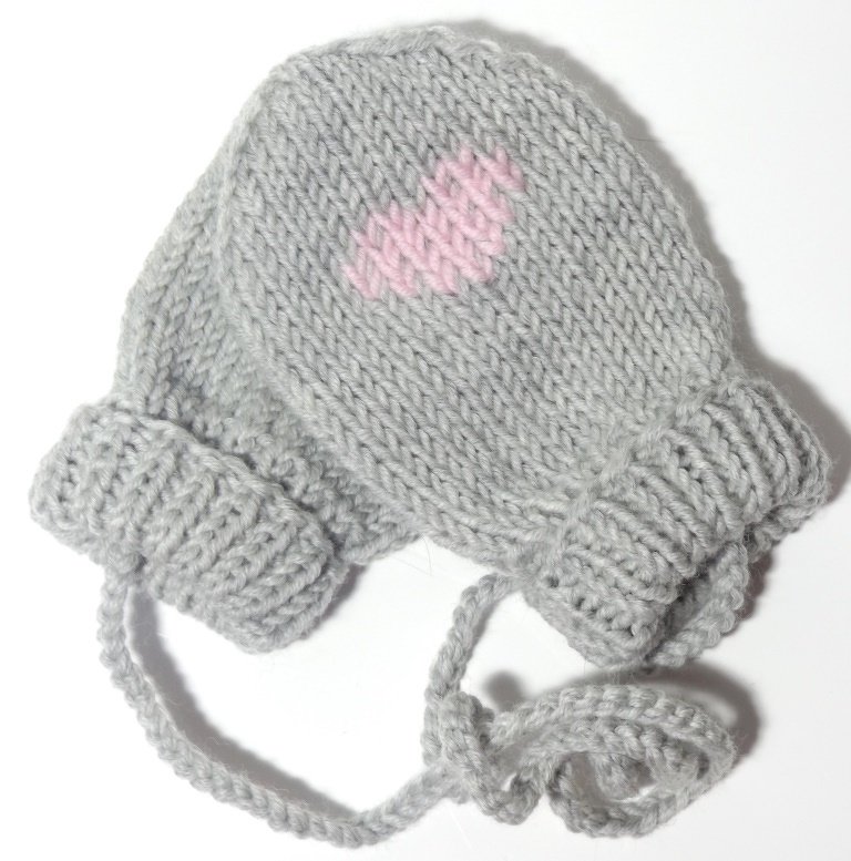Gestrickte hellgraue Babyfäustlinge mit rosa Herz und verbindender Kordel auf weißem Hintergrund