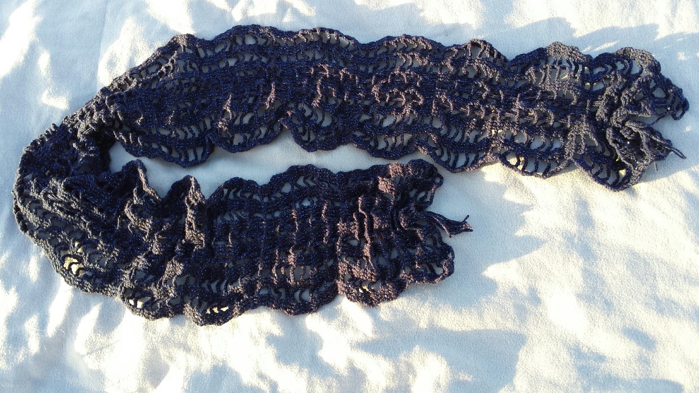 Gehäkelter dunkelblauer Schal mit glänzendem Garn und gewellter Kante auf hellem Untergrund.