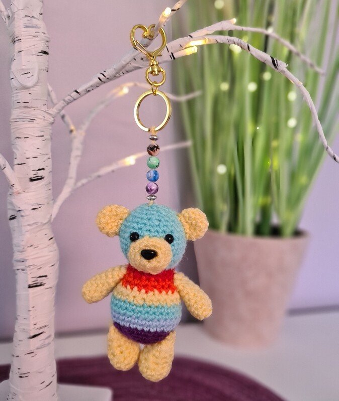 Gehäkelter Amigurumi-Teddy Schlüsselanhänger mit regenbogenfarbenem Körper und goldfarbenem Karabiner