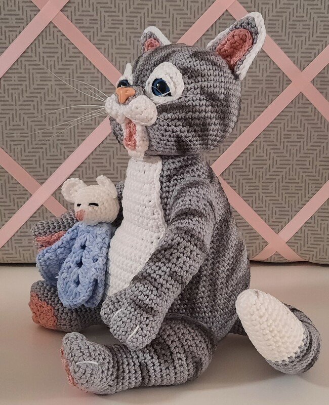 Sitzende grau-weiße Amigurumi-Katze mit blauen Augen und kleiner weißer Maus im blauen Tuch.