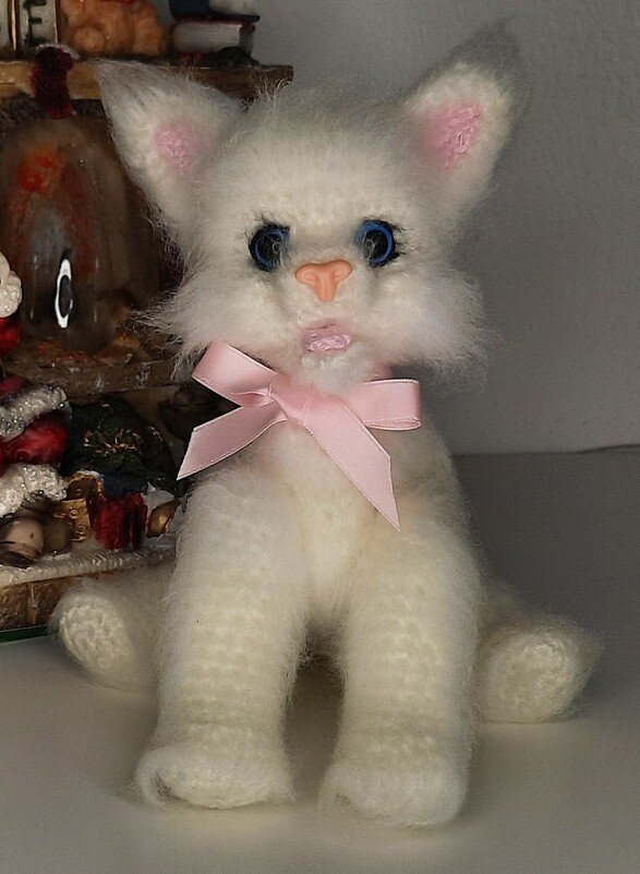 Weißes flauschiges Amigurumi-Kätzchen mit blauen Augen und rosa Schleife