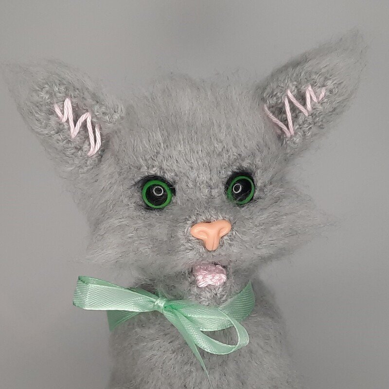 Grau gehäkelte Amigurumi
Katze mit grünen Augen, rosa Nase und mintgrünem Band