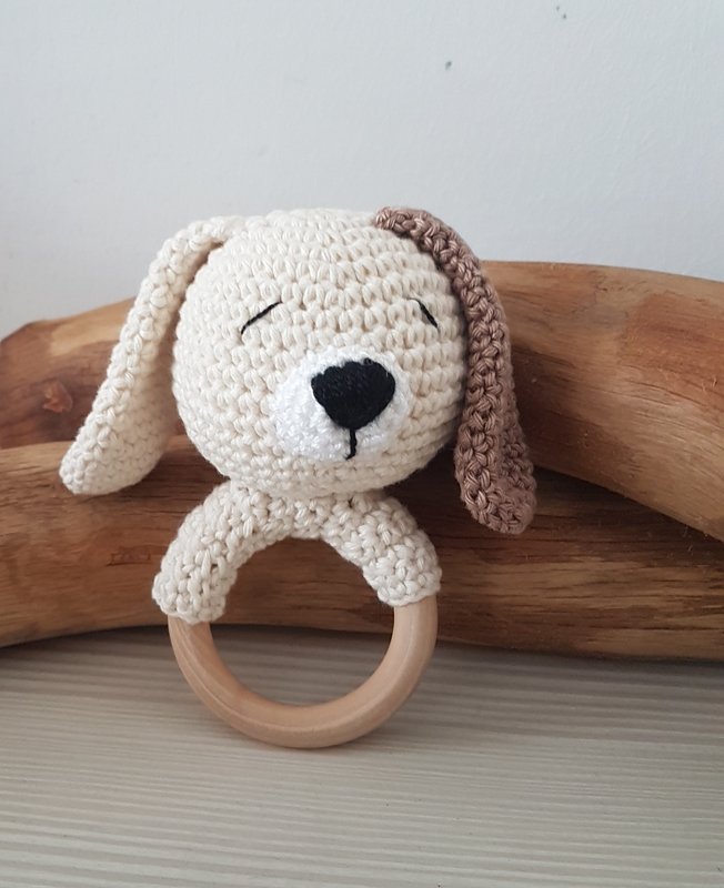 Gehäkelter cremefarbener Hund mit braunem Ohr und geschlossenen Augen, befestigt an einem Holzring.