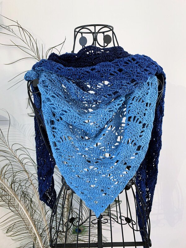 Crocheted triangle shawl with blue ombre design and openwork pattern displayed on a wire dress form.