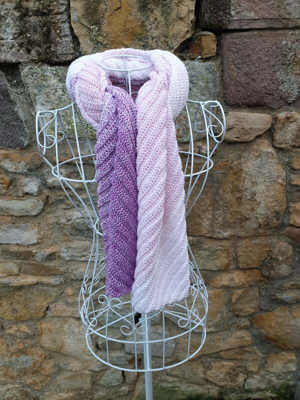 Gehäkelter Farbverlaufsschal (Lila-Rosé) mit Diagonalmuster auf weißer Drahtbüste vor Steinmauer