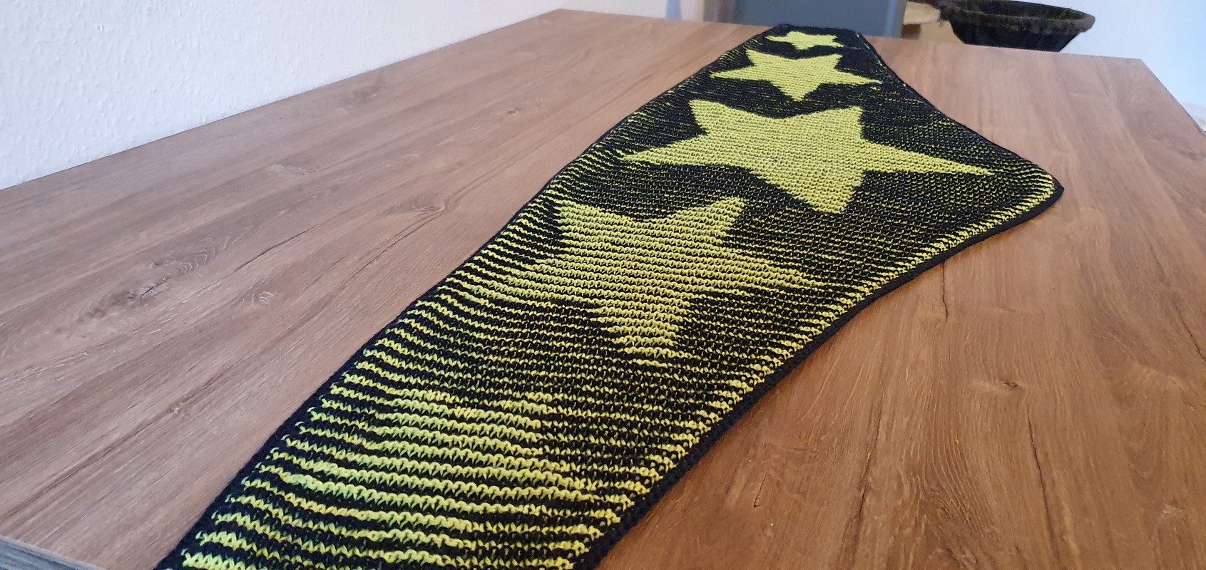 Black and yellow knitted shawl with large star motifs laid flat on a wooden table.