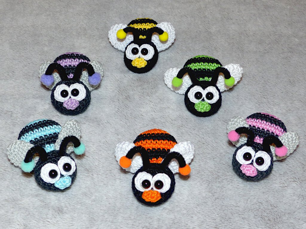 Six small striped crochet bee amigurumi motifs in different colors arranged on a gray surface