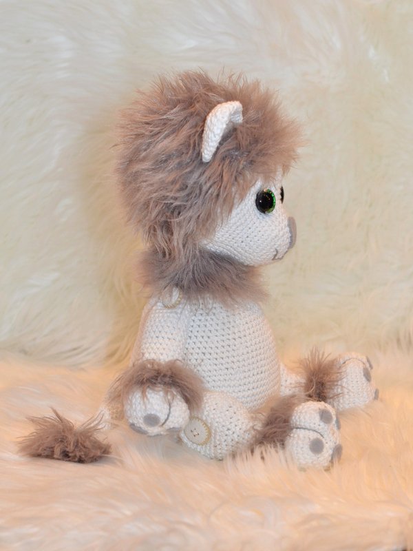 Gehäkeltes Amigurumi in Seitenansicht mit flauschiger Mähne und grünen Augen