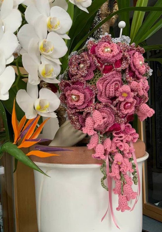 Gehäkelter Blumenstrauß in Pink- und Rosatönen mit Perlen, daneben weiße Orchideen