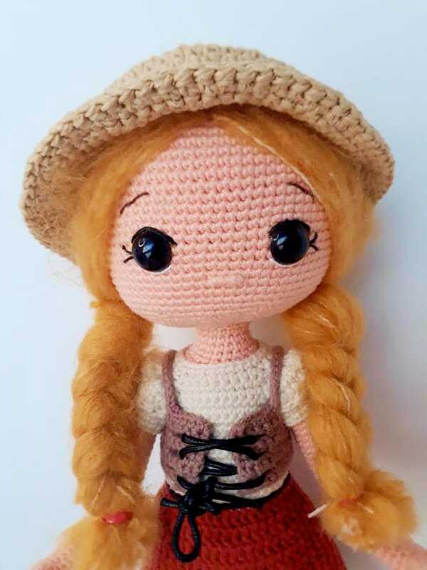 Handmade amigurumi doll with orange braided pigtails, beige crocheted hat, brown laced vest and red skirt