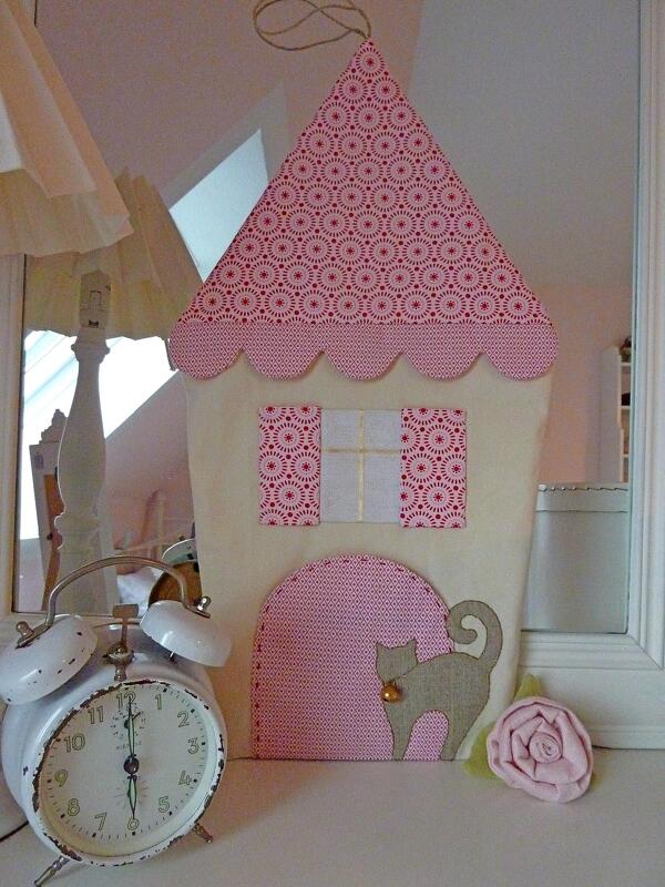 Genähtes Stoffhaus-Utensilo mit rosa gemustertem Dach, cremefarbenem Korpus, Fenstern und grauer Katze mit Glöckchen