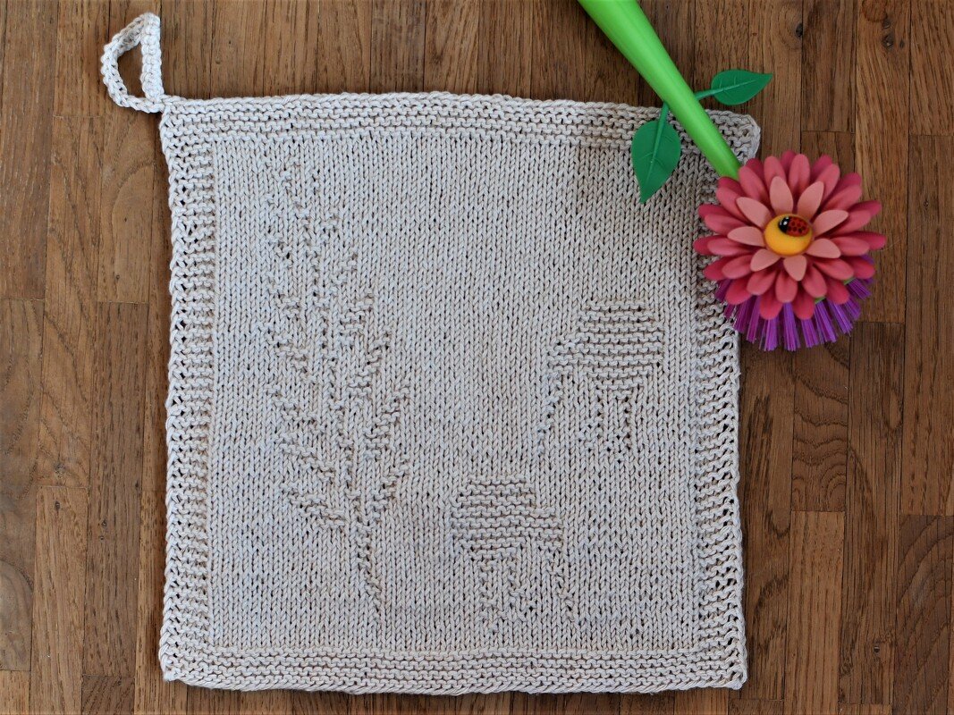Hellbeiges gestricktes Spültuch mit Blatt- und Pilzmuster und Aufhängeschlaufe auf Holzfußboden