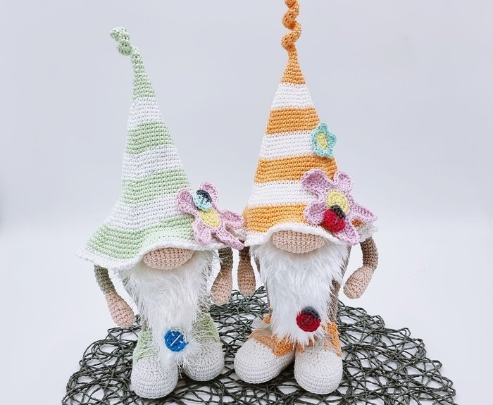 Zwei gehäkelte Amigurumi-Wichtel mit gestreiften Zipfelmützen und Blüten