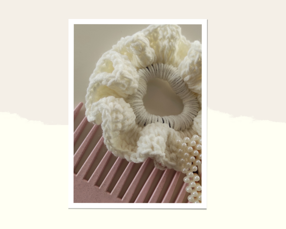 Cremefarbenes gehäkeltes Haargummi mit Rüschen auf rosa Kamm neben Perlen