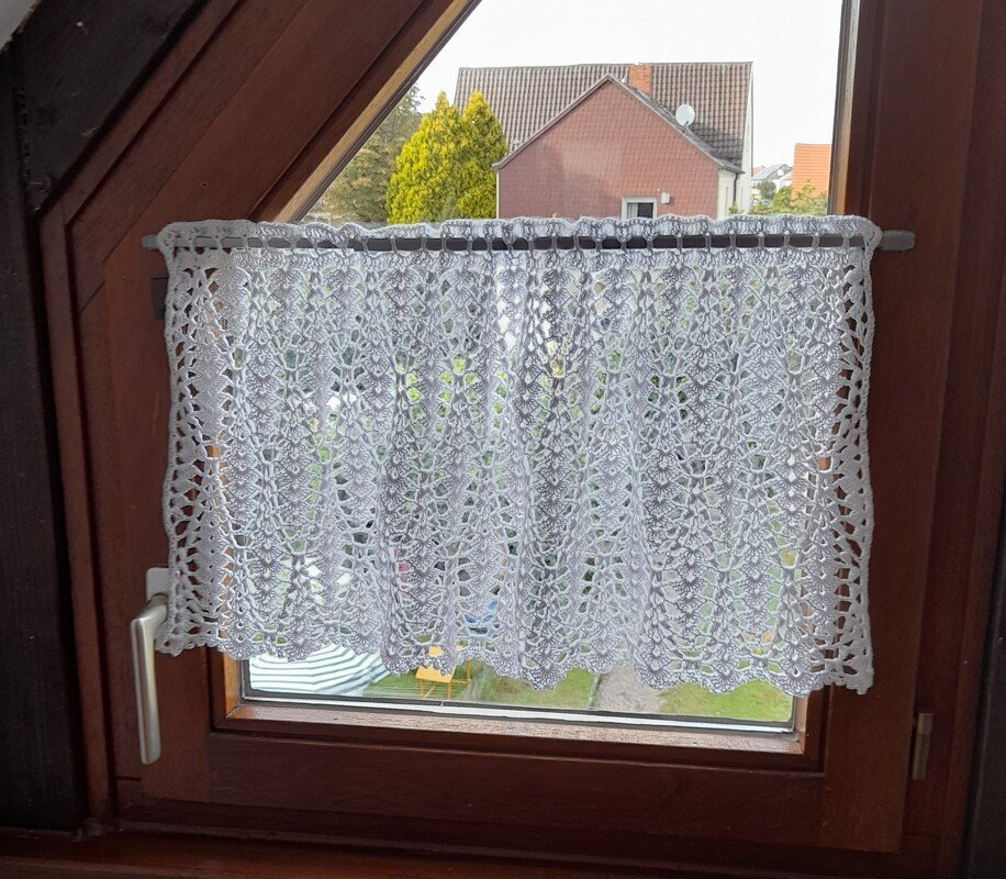 Weiße gehäkelte Scheibengardine mit Blatt- und Spitzenmuster an Holzfenster