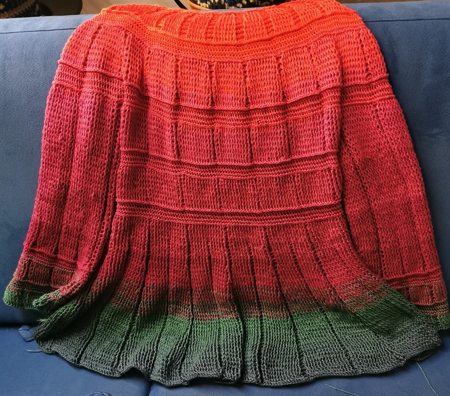 Gehäkelter Damenponcho in Rot bis Grün mit gestuften Paneelen und Rippstruktur, auf einer Couch drapiert