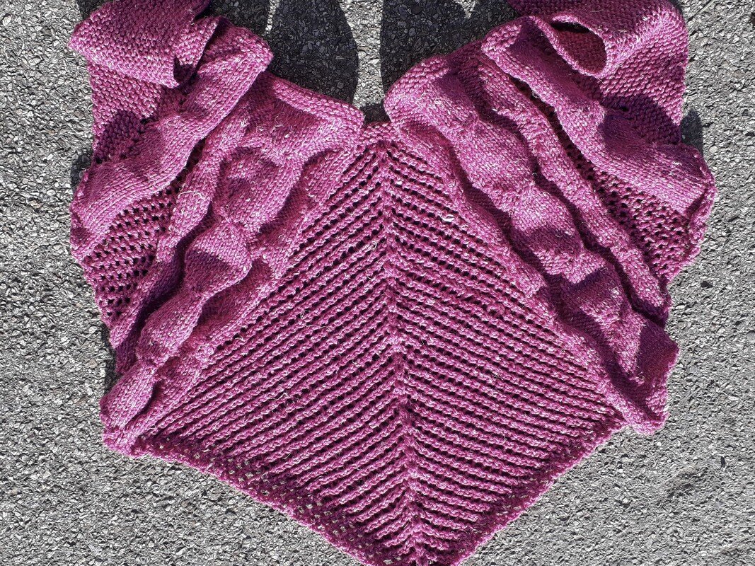 Magenta knitted triangle shawl with chevron and textured stitch panels on pavement