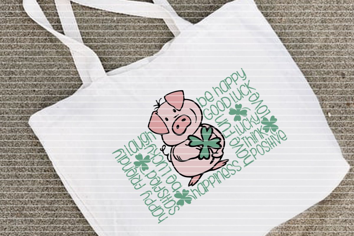 Weiße Stofftasche mit rosa Schwein, das ein Kleeblatt hält, umgeben von englischen Glückswörtern