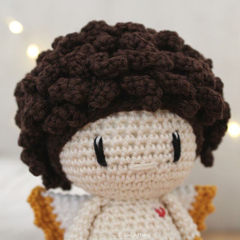 Gehäkeltes Amigurumi-Engelchen mit dunklen Locken, cremefarbenem Körper und Flügeln mit senfgelbem Rand