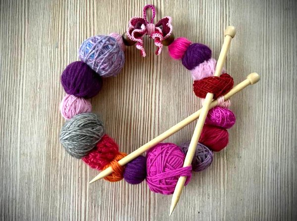 Kranz aus bunten Wollknäueln mit gekreuzten Stricknadeln und Häkelschleife