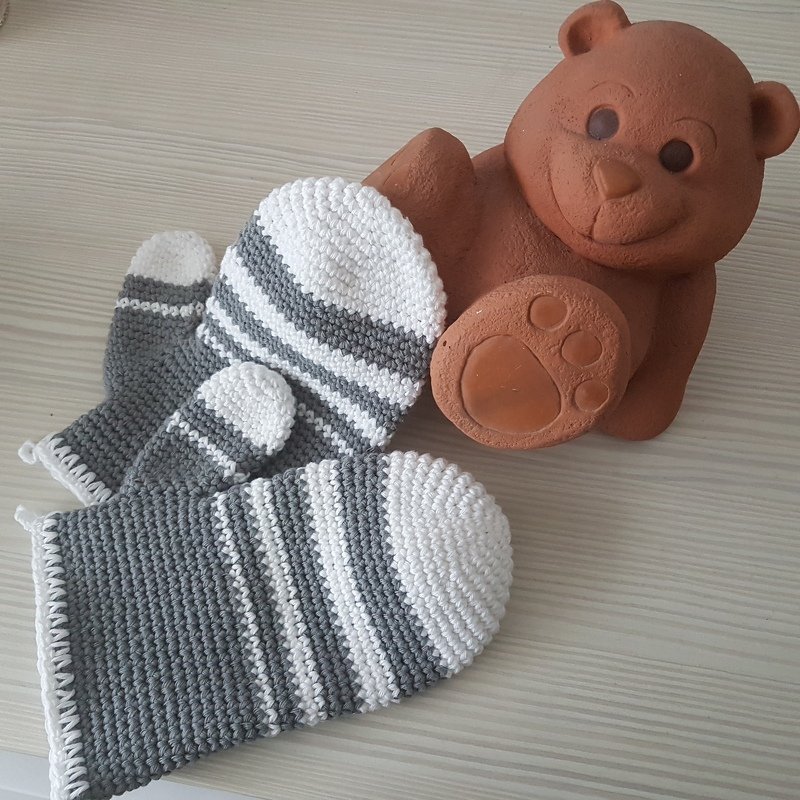 Gehäkelte graue und weiße Topflappen mit Streifen neben einer Tonbärenfigur