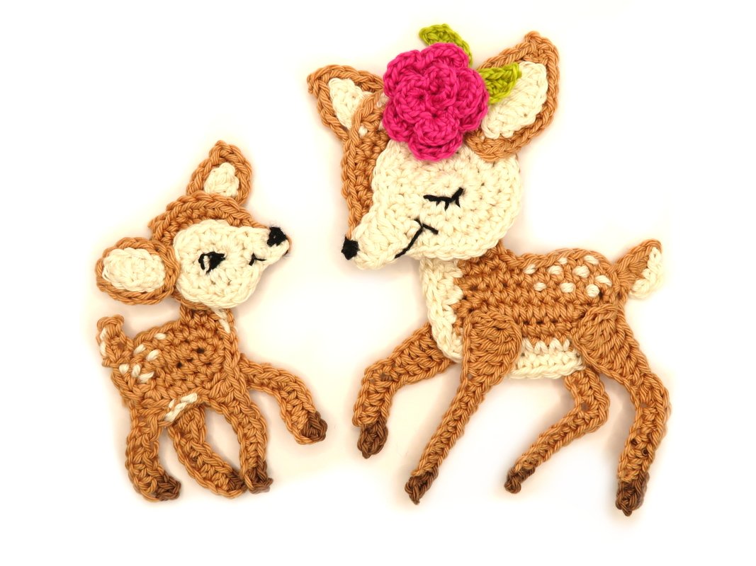 Flat-lay of two crocheted fawn appliqués in tan and cream, larger fawn with pink flower, showing stitch detail and scale