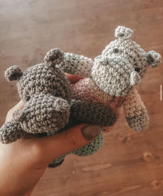 Hand hält zwei gehäkelte Mini-Nilpferd-Amigurumi in Grau und Rosa