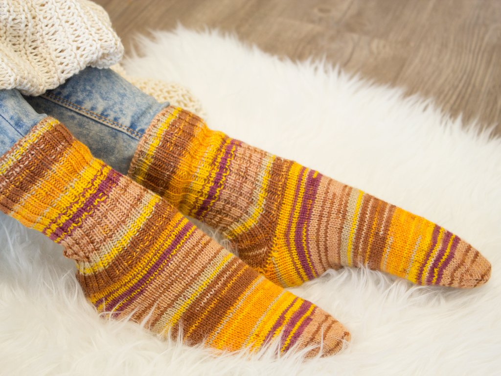 Gestrickte gestreifte Socken in Gelb, Braun und Violett auf weißem Teppich