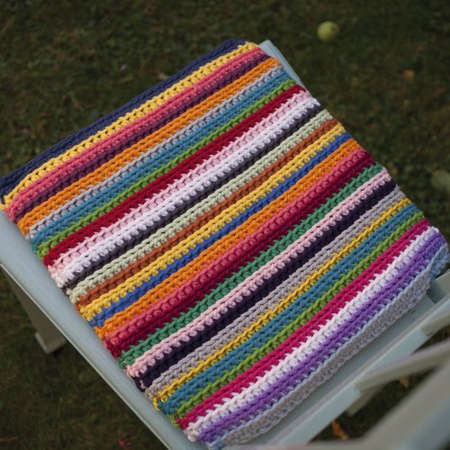 Gehäkeltes Quadrat mit bunten Streifen, gefaltet auf einem Stuhl