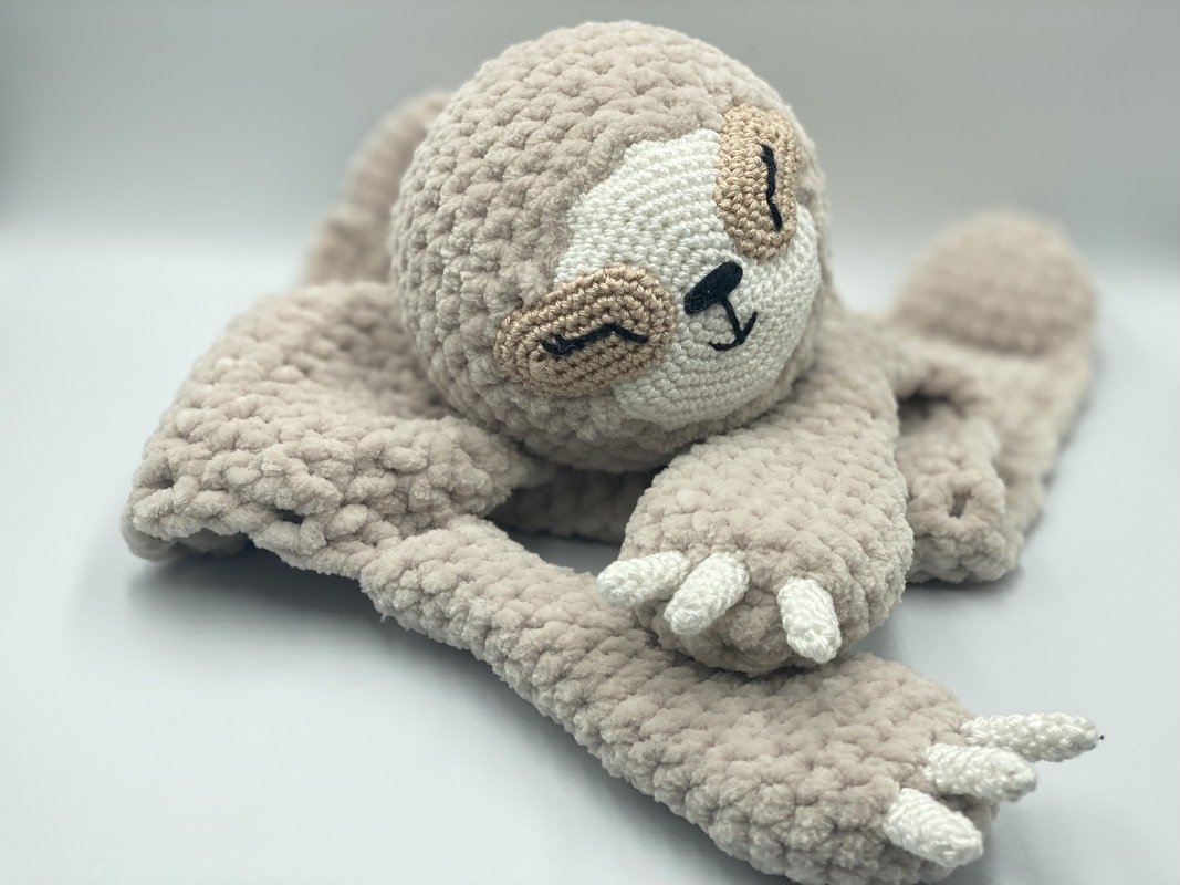 Beige crocheted sloth lovey with embroidered sleepy face and plush textured blanket
