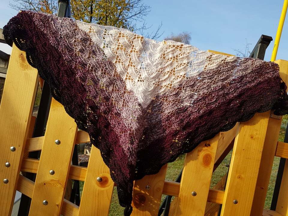 Gehäkeltes Dreieckstuch mit Farbverlauf von Burgund zu Creme, filigranes Spitzenmuster, auf Holzgeländer drapiert
