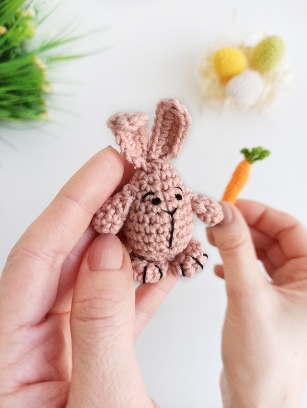 Hands holding a small pink crocheted bunny and a tiny orange crocheted carrot.