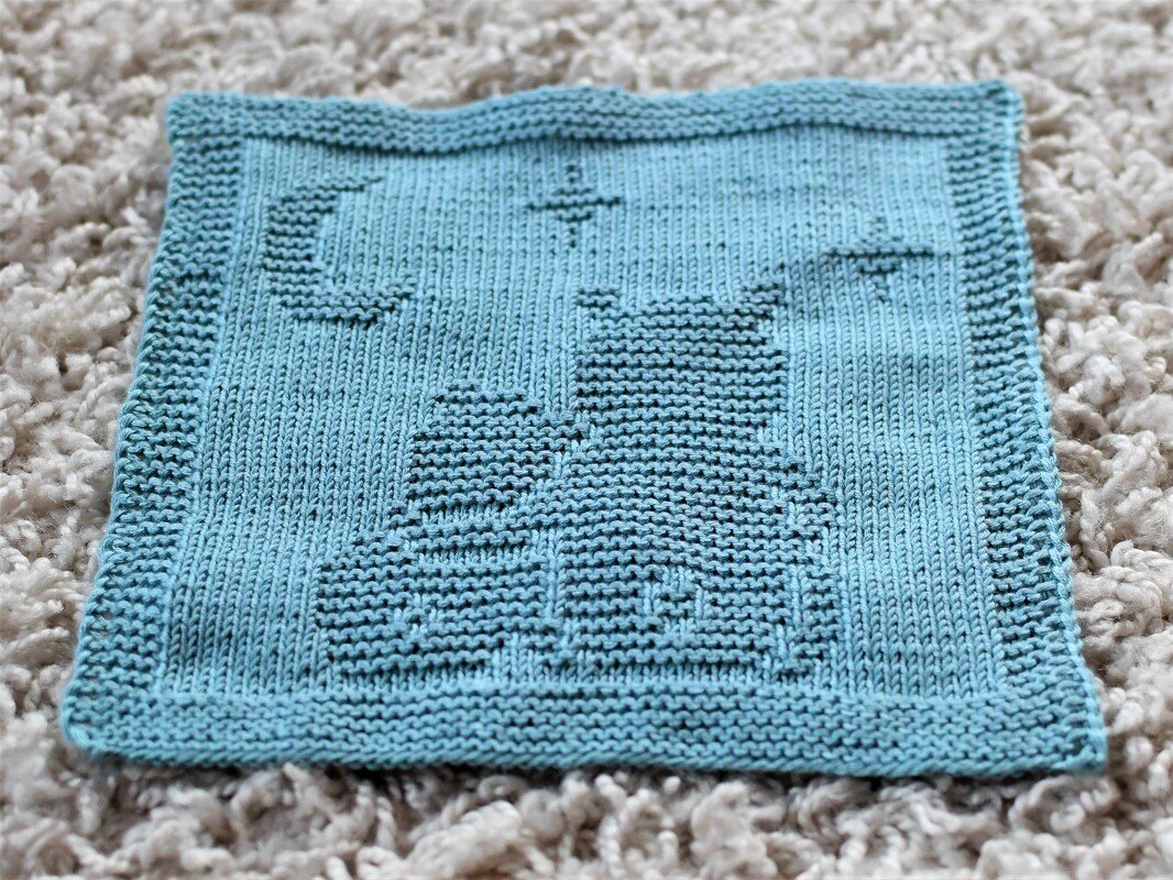 Light blue knitted square with garter-stitch cat silhouette, crescent moon and star
