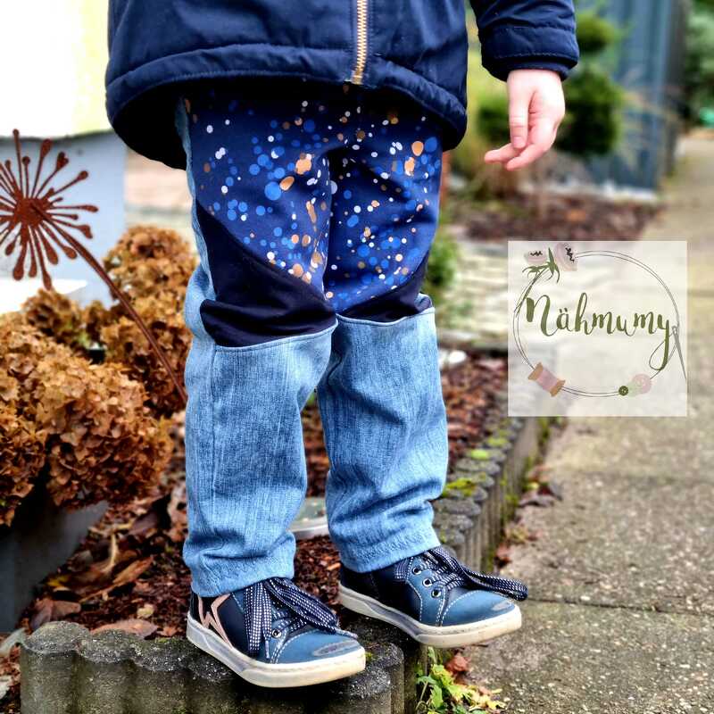 Beine eines Kindes in zweifarbiger Kinderhose mit Punktemuster oben und jeansähnlichem Stoff unten, blaue Sneaker