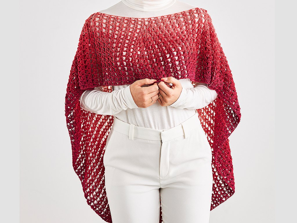 Gehäkelter roter Poncho mit Farbverlauf und Lochmuster über weißer Kleidung.