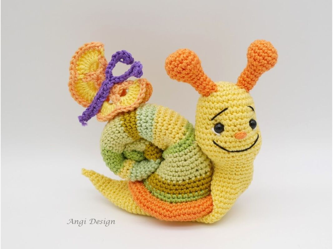 Gehäkelte Amigurumi-Schnecke in Gelb, Grün und Orange mit kleinem Schmetterling auf dem Haus