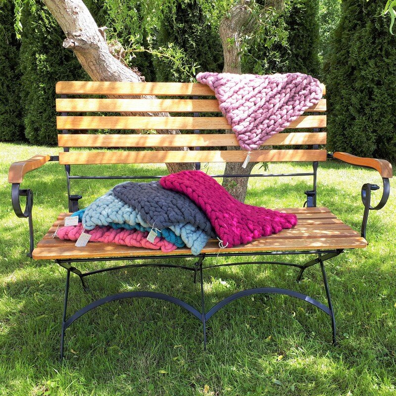 Bunte grob gestrickte Decken auf einer Holzbank im Garten