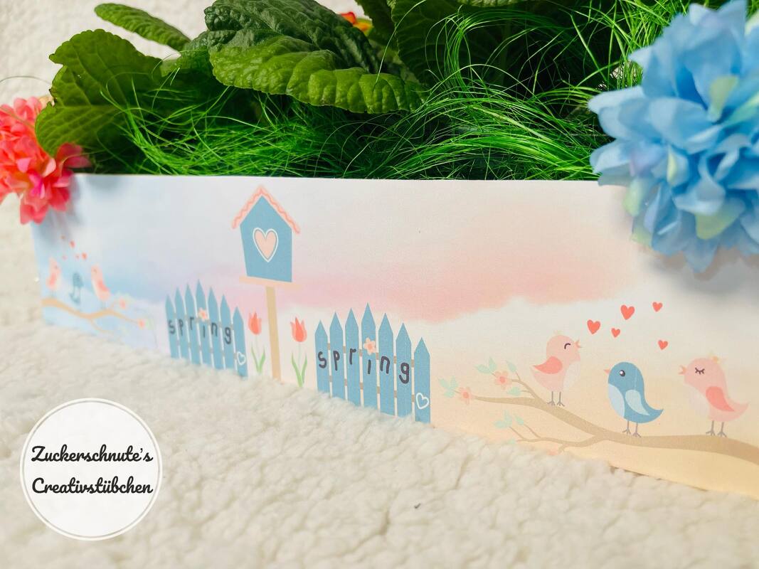 Pastellfarbene Frühlingsillustration mit Vogelhaus, blauem Lattenzaun mit dem Schriftzug SPRING, Tulpen und drei Vögeln auf einem Ast.