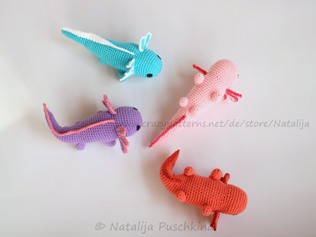 four crocheted amigurumi axolotls in turquoise, pink, purple and coral on white background