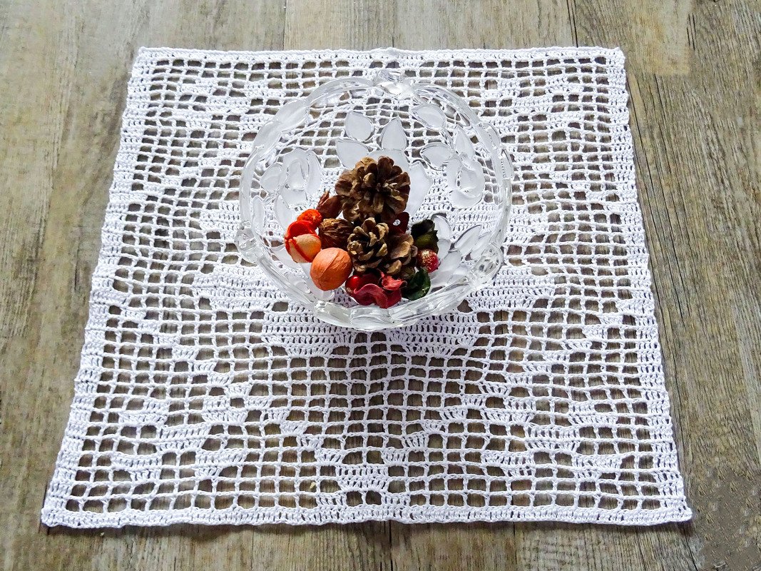 Quadratisches weißes gehäkeltes Filetdeckchen auf Holztisch mit Glasschale und getrockneten Deko-Elementen