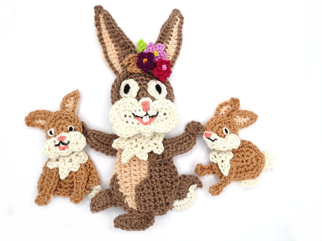 Three crocheted bunny appliqués on white background - one large floral-crowned rabbit and two smaller bunnies