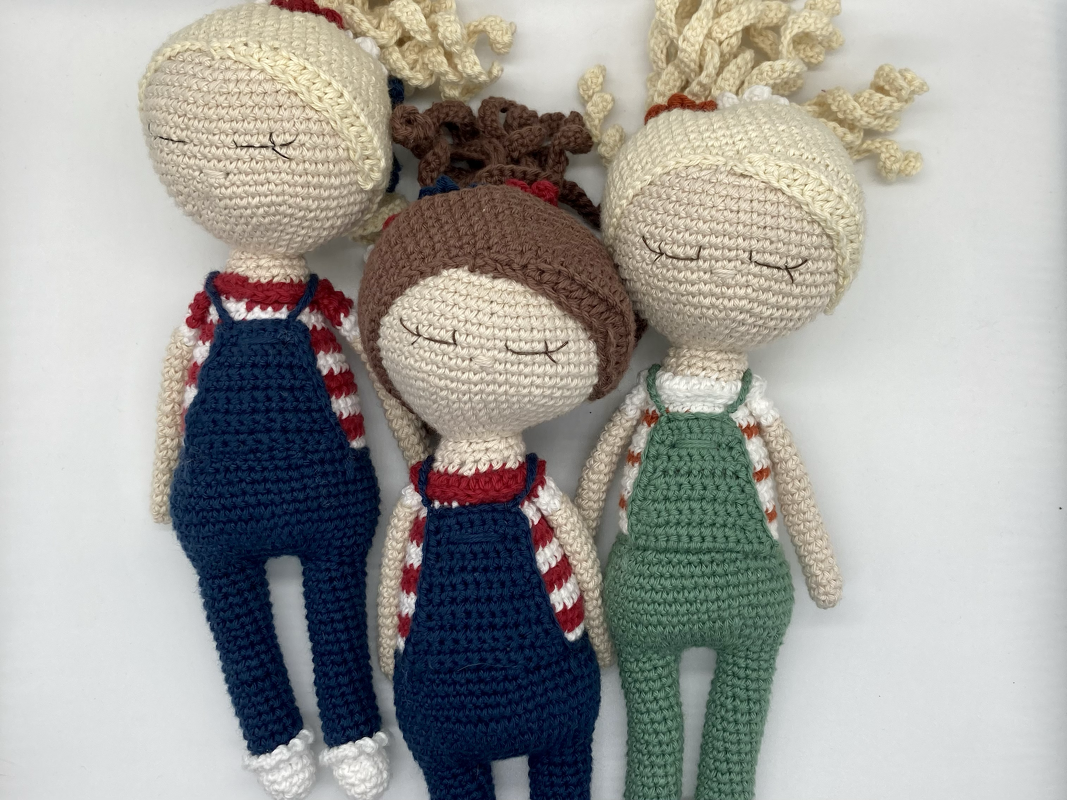 Nahaufnahme von drei gehäkelten Amigurumi-Puppen mit Fokus auf Augen, Latzhosen und Frisuren