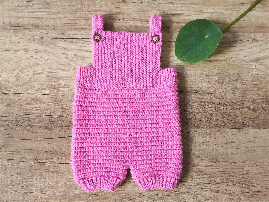 Rosa gehäkelter Babystrampler mit Holzknöpfen auf Holzuntergrund