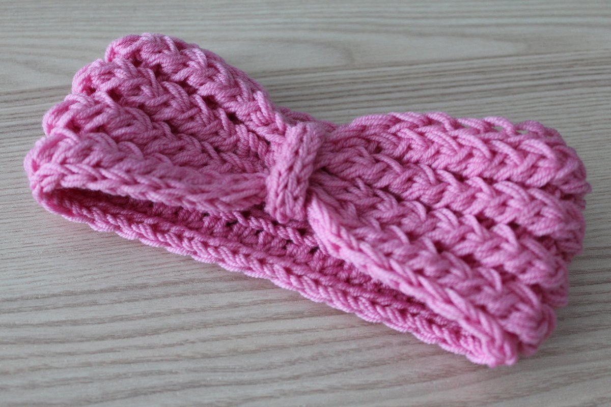 Rosa gestricktes Stirnband mit Knoten auf hellem Holzhintergrund