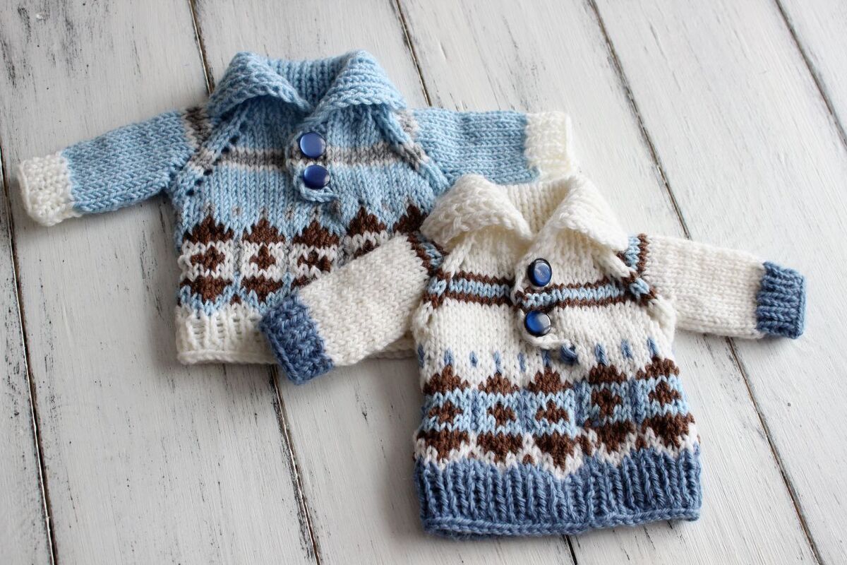 Flat-lay of two small patterned knitted sweaters with ribbing, turned collars and blue buttons on white wooden planks