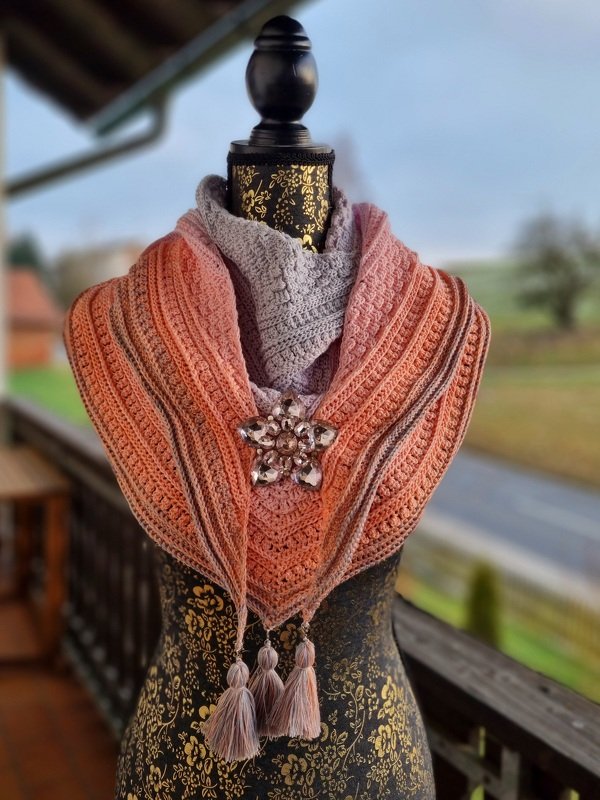 Gehäkeltes Dreieckstuch in Grau, Rosa und Orange mit Brosche und Quasten auf einer Schneiderpuppe