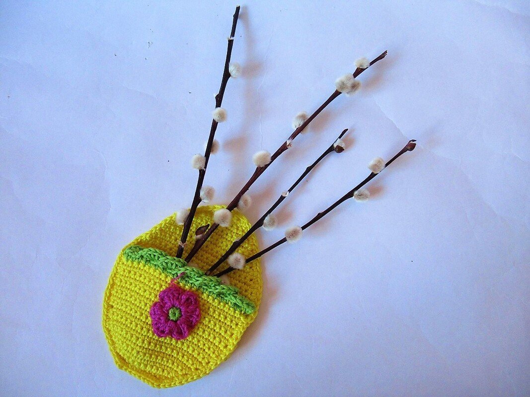 Gehäkeltes gelbes Osterkörbchen mit grüner Borte, pinker Blume und Weidenkätzchenzweigen