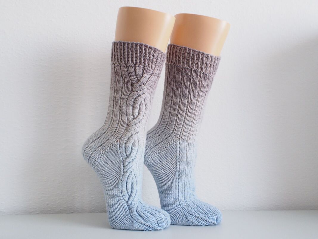 Pair of women's mid-calf socks in taupe-to-blue ombre with ribbed cuffs and decorative cable along the instep, displayed on sock forms